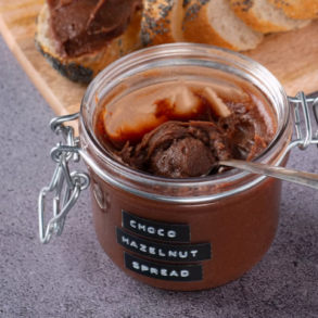 A jar of chocolate hazelnut spread with bread covered in the spread n the background. Image by Max Griss from Unsplash
