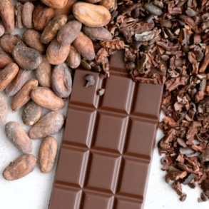 Image of a chocolate bar with cocoa beans on one side and cocoa nibs on the other against a white background. Image by Tetiana Bykovets on Unsplash