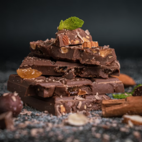 A pile of chocolate bars with various inclusions broken and assembled artistically with a leaf on top. Image by Pushpak Dsilva on Unsplash